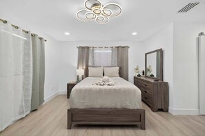 A bedroom with a bed, bedside tables, a dresser, a mirror, and a modern ceiling light fixture. - Central Tampa 3BR/2BA • Near Stadium & Airport (Tampa)