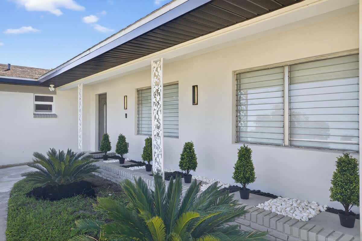 A modern house with a covered porch, potted plants, and a clear sky.