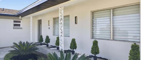 A modern house with a covered porch, potted plants, and a clear sky.
