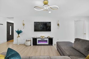 A modern living room with a grey sofa, a fireplace, a mounted TV, and a decorative wall piece. - Central Tampa 3BR/2BA • Near Stadium & Airport (Tampa)
