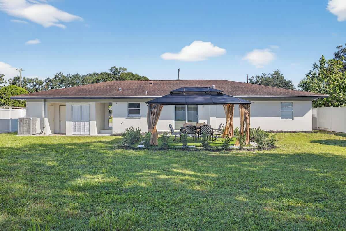A single-story house with a covered patio area, a lawn, and a clear sky.