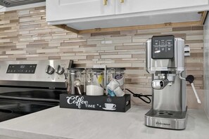 Uma cozinha moderna com cafeteira, balança digital e espaço para café com xícaras e vaporizador de leite.