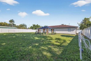 A residential property with a well-maintained lawn, a patio with chairs, and a house with a red roof. - Central Tampa 3BR/2BA • Near Stadium & Airport (Tampa)