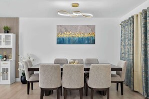 Ein Essbereich mit Tisch und Stühlen, einer Deckenleuchte, einem Wandbild und einem Vorhang.