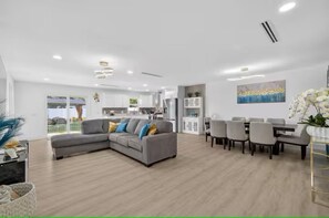 Ein modernes Wohnzimmer mit Ecksofa, Essbereich mit Stühlen und einer Küche im Hintergrund.