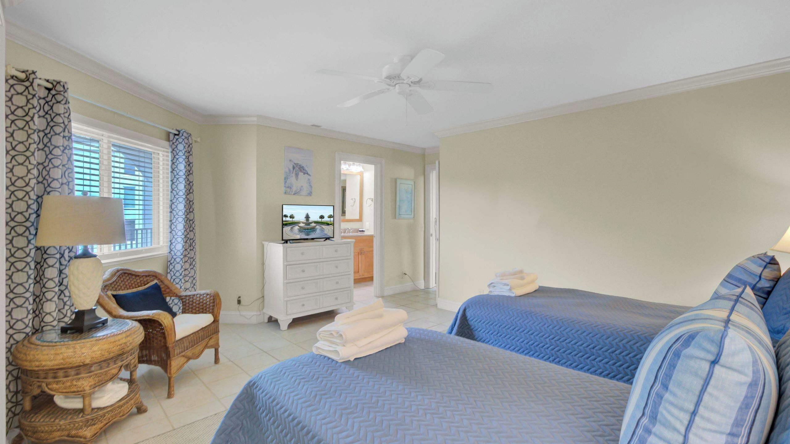 A bedroom with two beds, a chair, a dresser, a television, and a ceiling fan.