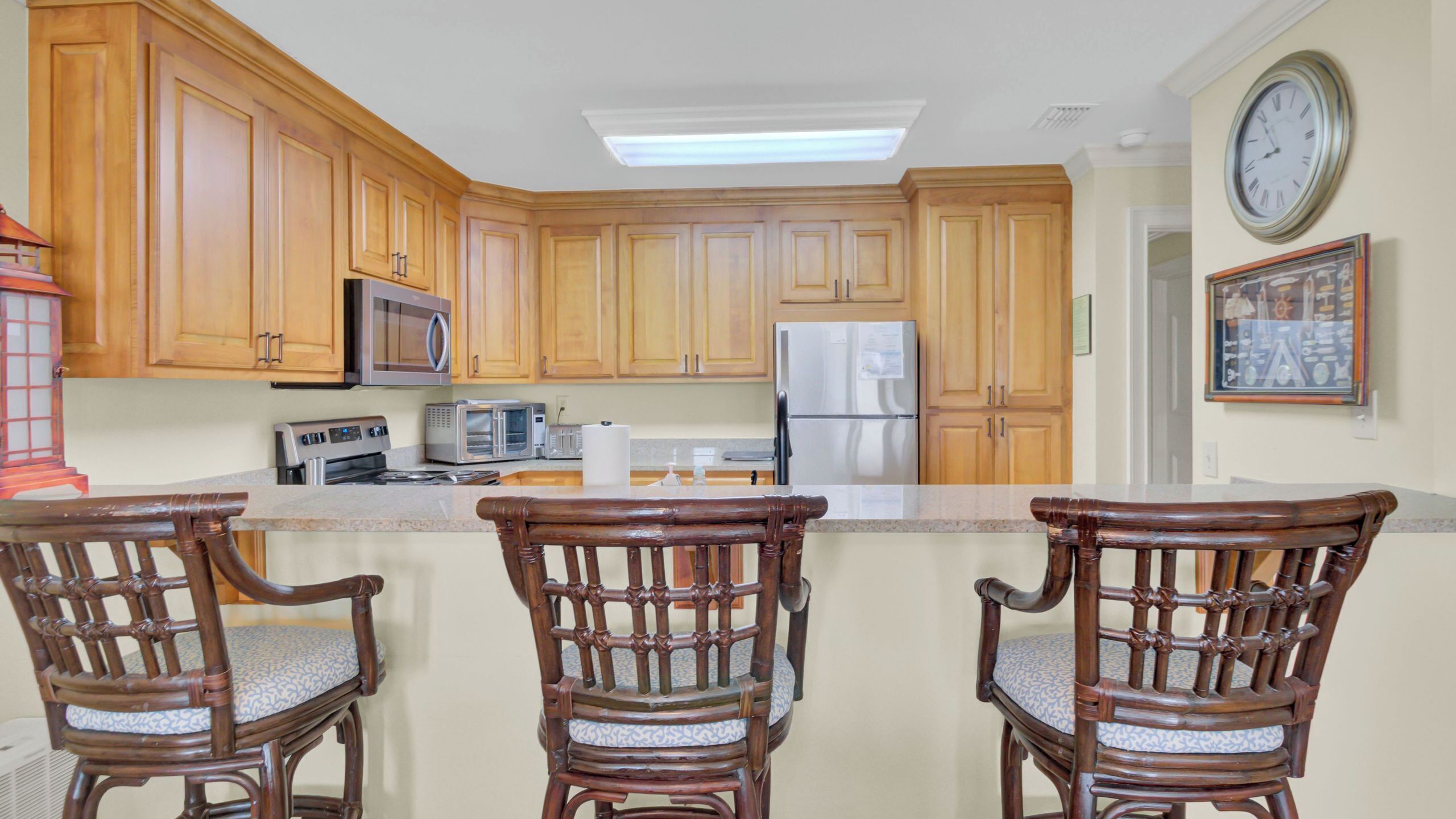 A kitchen with wooden cabinets, a microwave, a toaster, a refrigerator, and a clock on the wall.