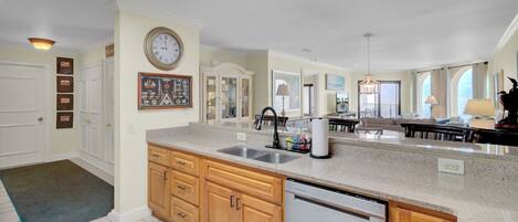 A kitchen with wooden cabinets, a stainless steel sink, a dishwasher, and a large wall clock.