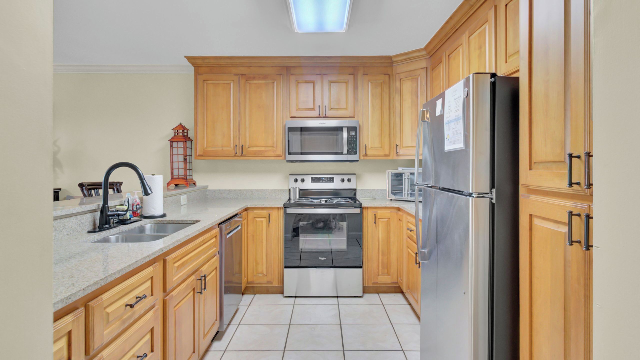 A kitchen with wooden cabinets, a stainless steel refrigerator, a microwave, an oven, and a sink.
