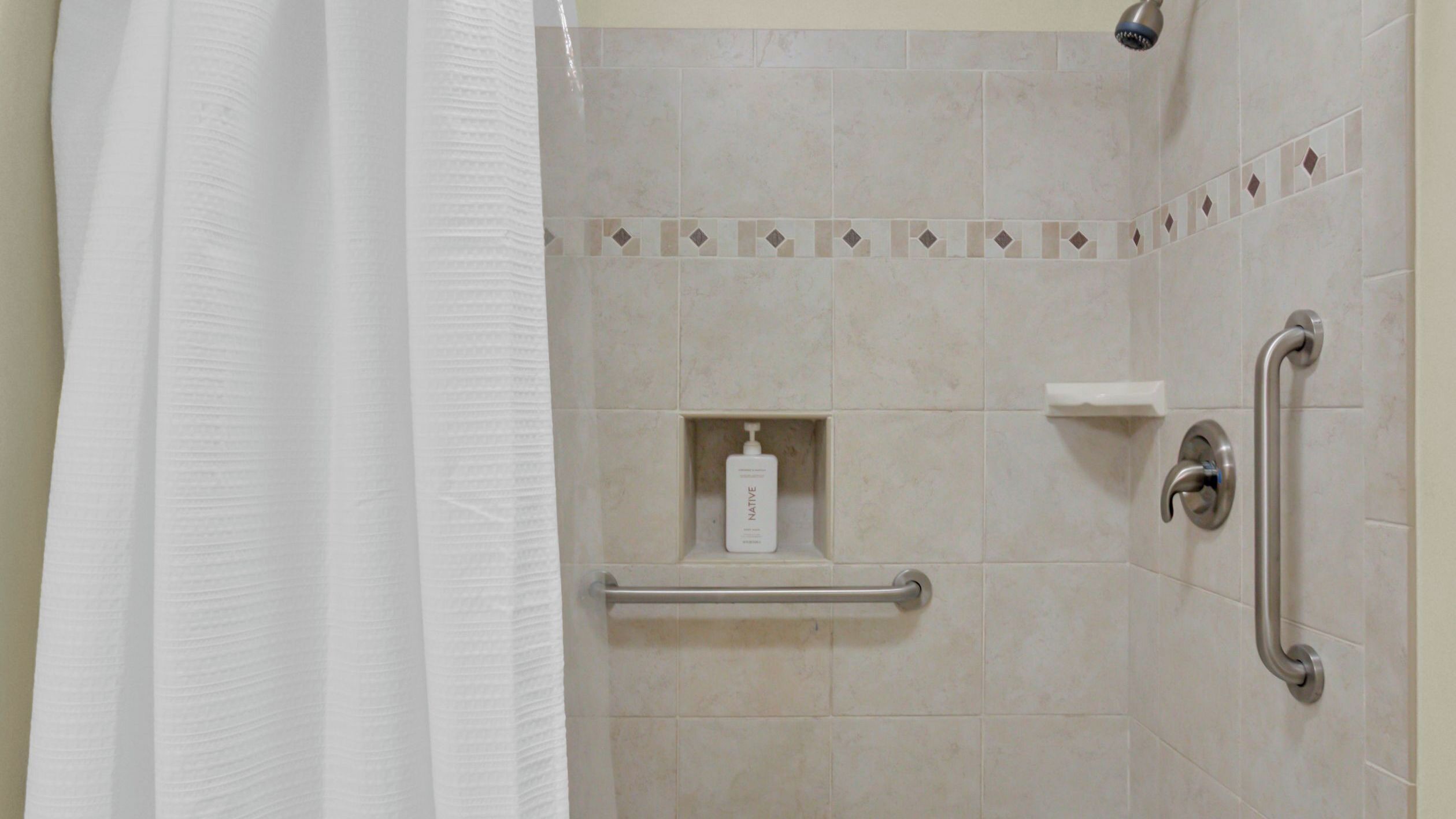 A shower area with a handrail, a shelf with a bottle, and a towel rack.