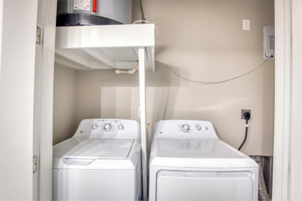 A laundry room with two white front-loading washing machines, a white ceiling-mounted dryer, and a visible electrical outlet on the wall.