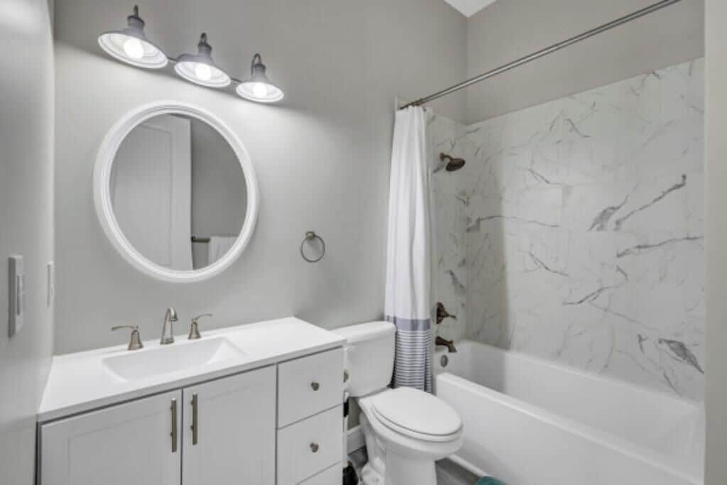A bathroom with a white sink, round mirror, and a shower curtain.