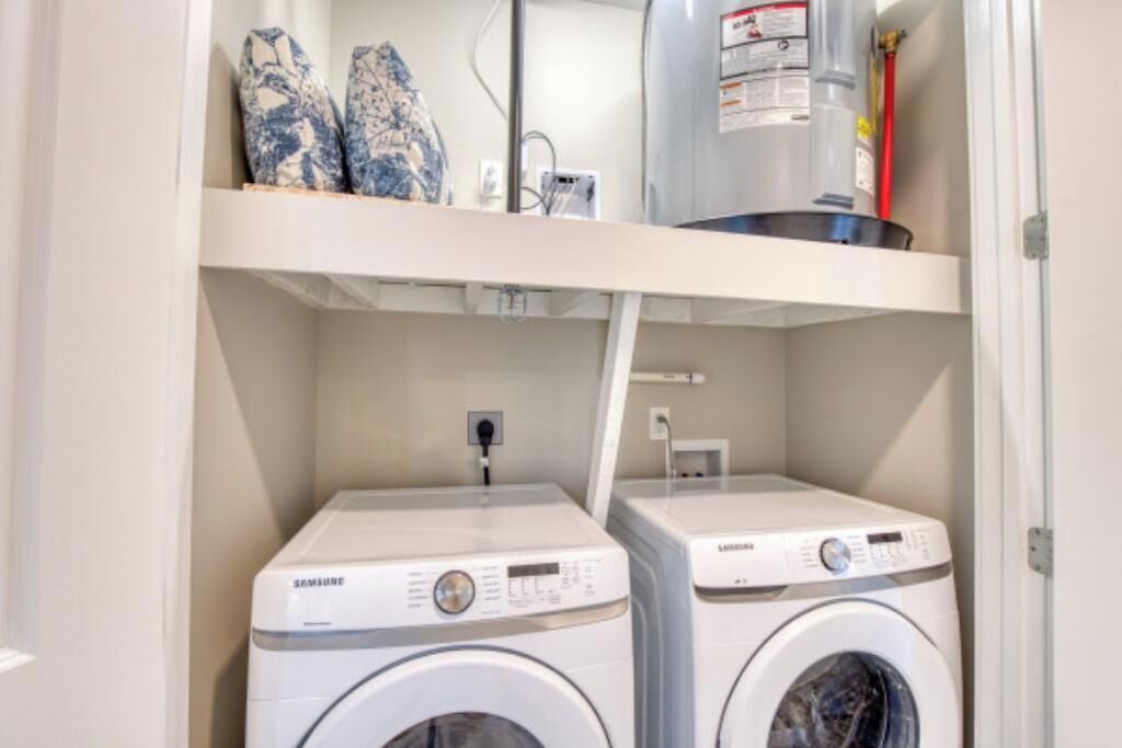 A laundry area with two Samsung washing machines and a shelf above containing a fire extinguisher and some decorative items.
