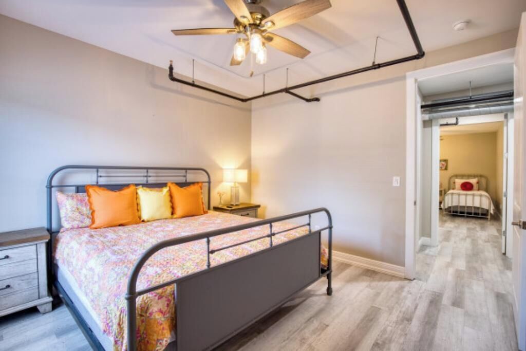 Une chambre à coucher comprenant un lit, une table de chevet, un ventilateur de plafond et un couloir menant à une autre pièce.
