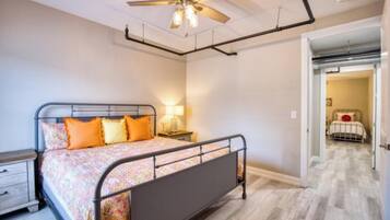Une chambre à coucher comprenant un lit, une table de chevet, un ventilateur de plafond et un couloir menant à une autre pièce.