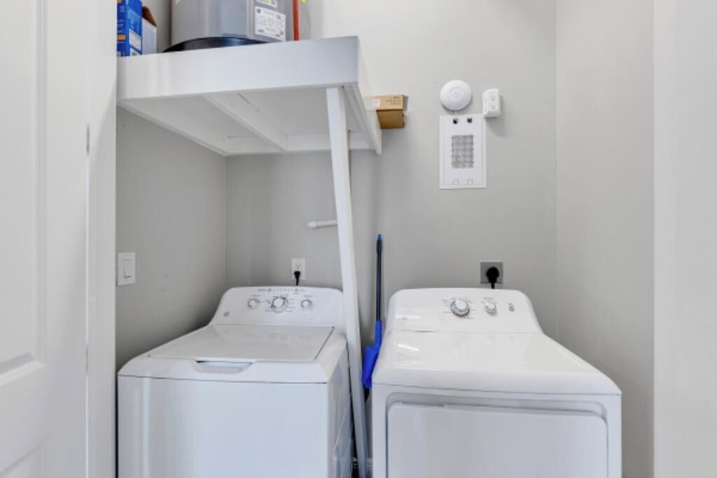 A laundry room with two white washing machines, a blue mop, and a wall-mounted electrical outlet.
