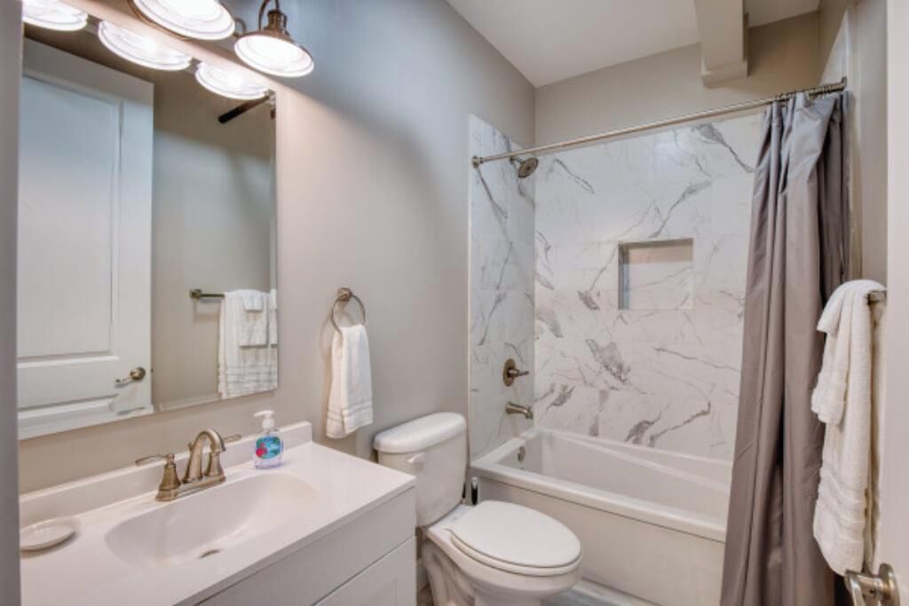 A bathroom with a white sink, toilet, and bathtub with a marble shower wall.