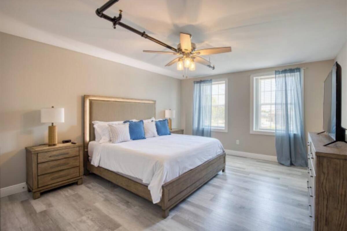 Un dormitorio con cama, mesitas de noche, ventilador de techo y cómoda.