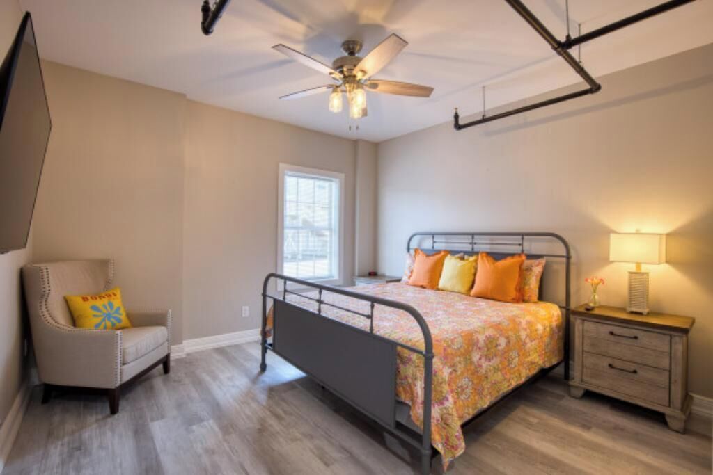 A bedroom with a bed, a chair, a nightstand, a ceiling fan, and a window.