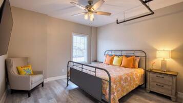 A bedroom with a bed, a chair, a nightstand, a ceiling fan, and a window.