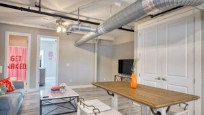 A modern living room with a wooden dining table, white sofas, and a TV. - 902 Howard Lofts (Biloxi)