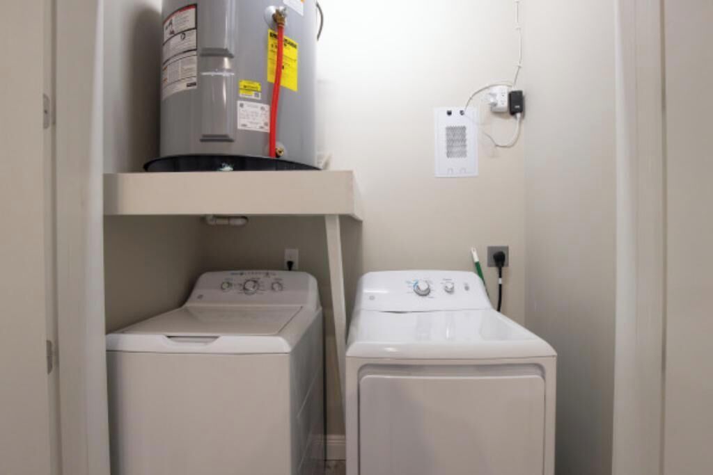 A laundry room with a washer and dryer, a water heater, and a wall outlet.