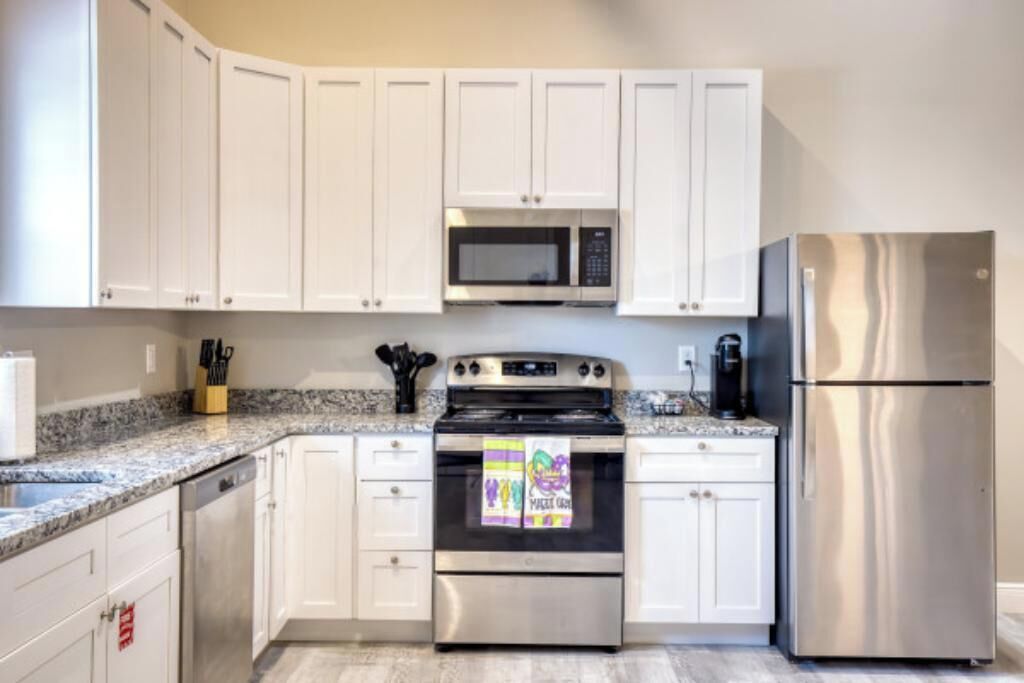 Una cocina con armarios blancos, un refrigerador de acero inoxidable, un microondas y una estufa.