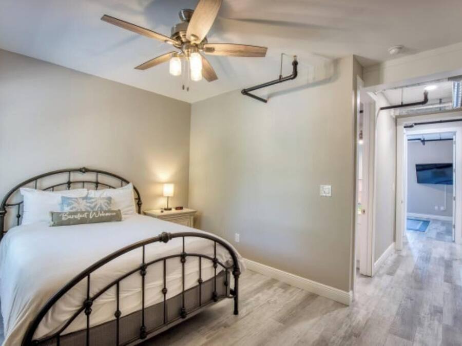 Een slaapkamer met een bed, een plafondventilator, een nachtkastje en een deur naar een andere kamer.