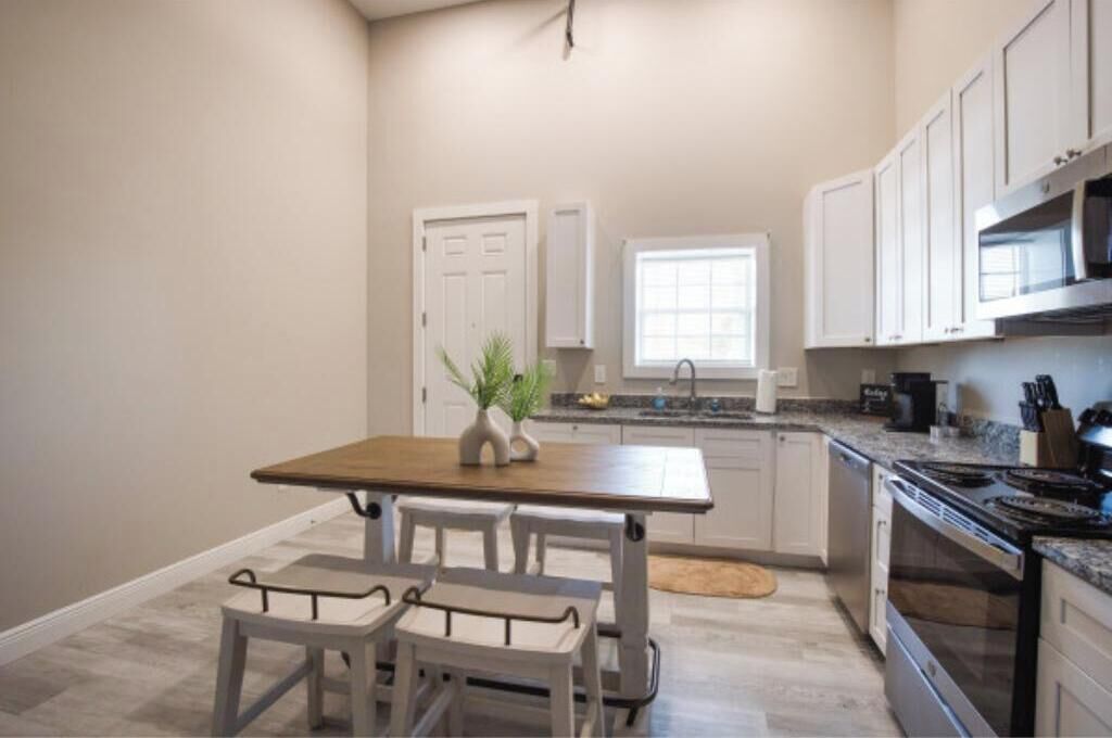 Una cocina con armarios blancos, una mesa de madera y un ventanal.