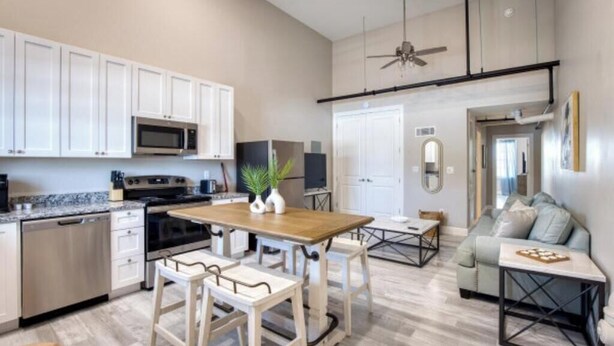 A modern kitchen with white cabinets, a microwave, and a dining area with a wooden table and chairs. - 902 Howard Lofts (Biloxi)