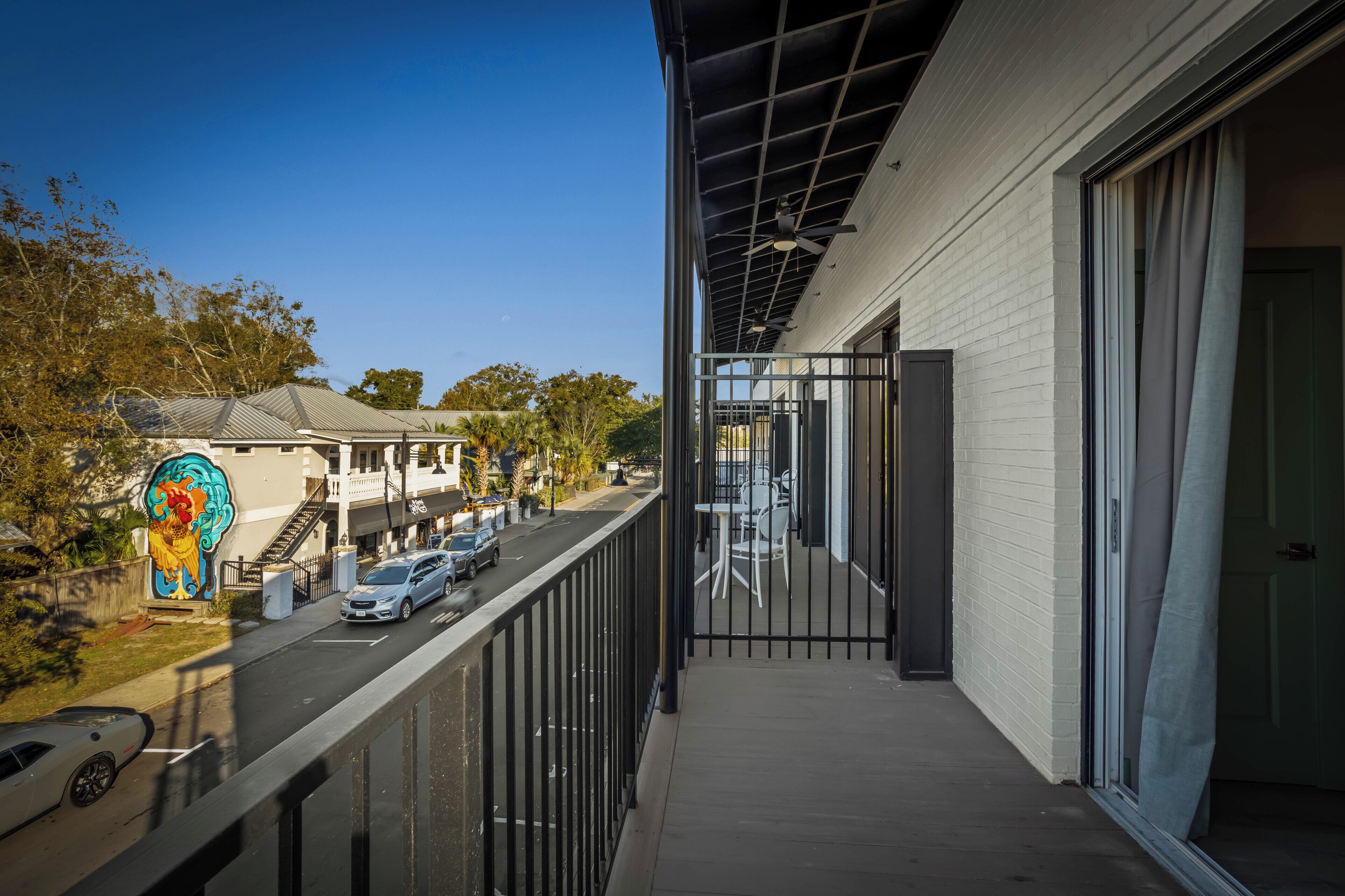 A balcony with a view of a street, a building with a mural, and a clear blue sky.