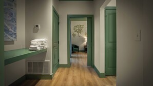 A hallway with a green door, a white wall with a thermostat, and a stack of white towels on a green shelf. - Hotel Mojo (Ocean Springs)