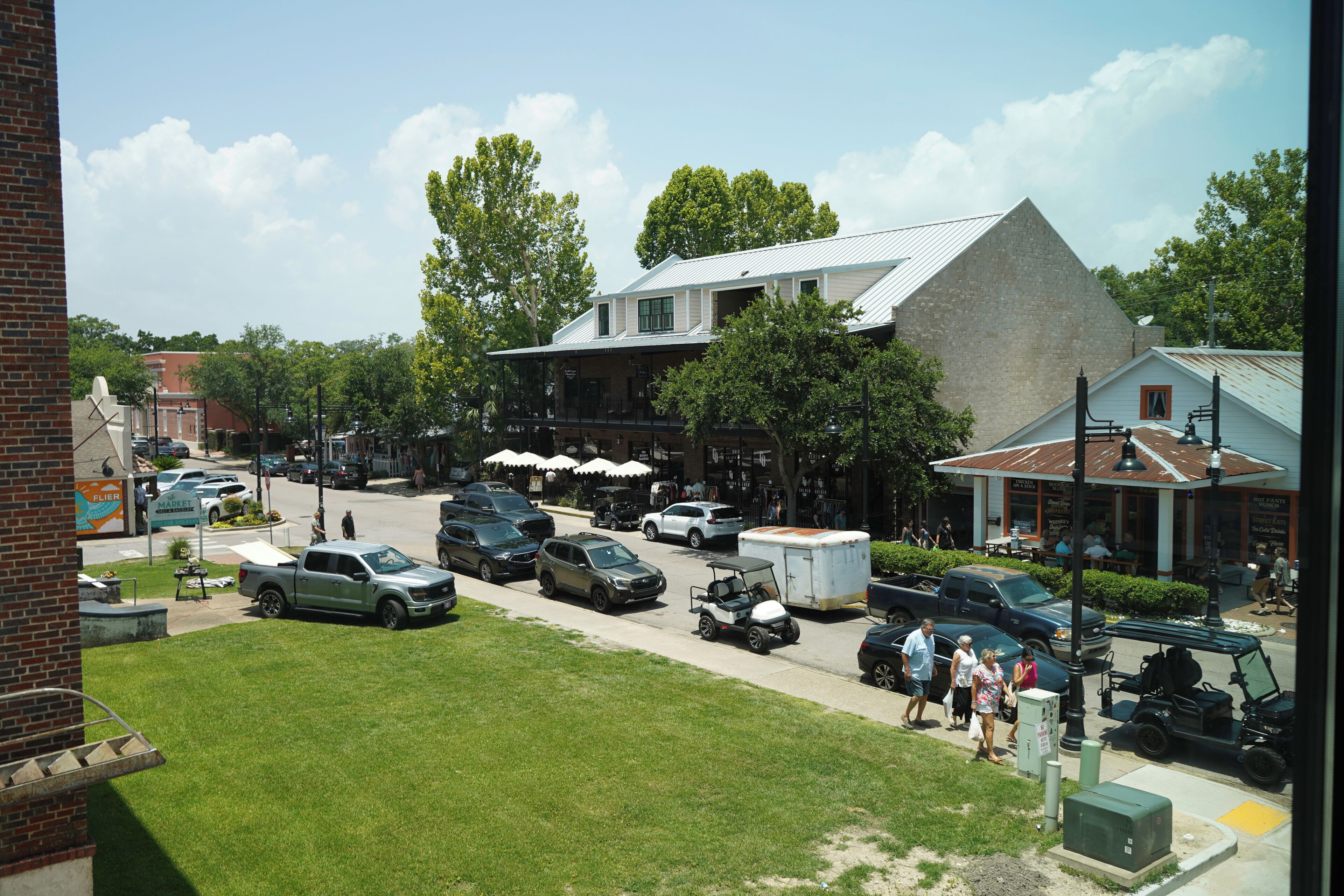 A parking lot with various vehicles, a building with a sloped roof, and a grassy area.