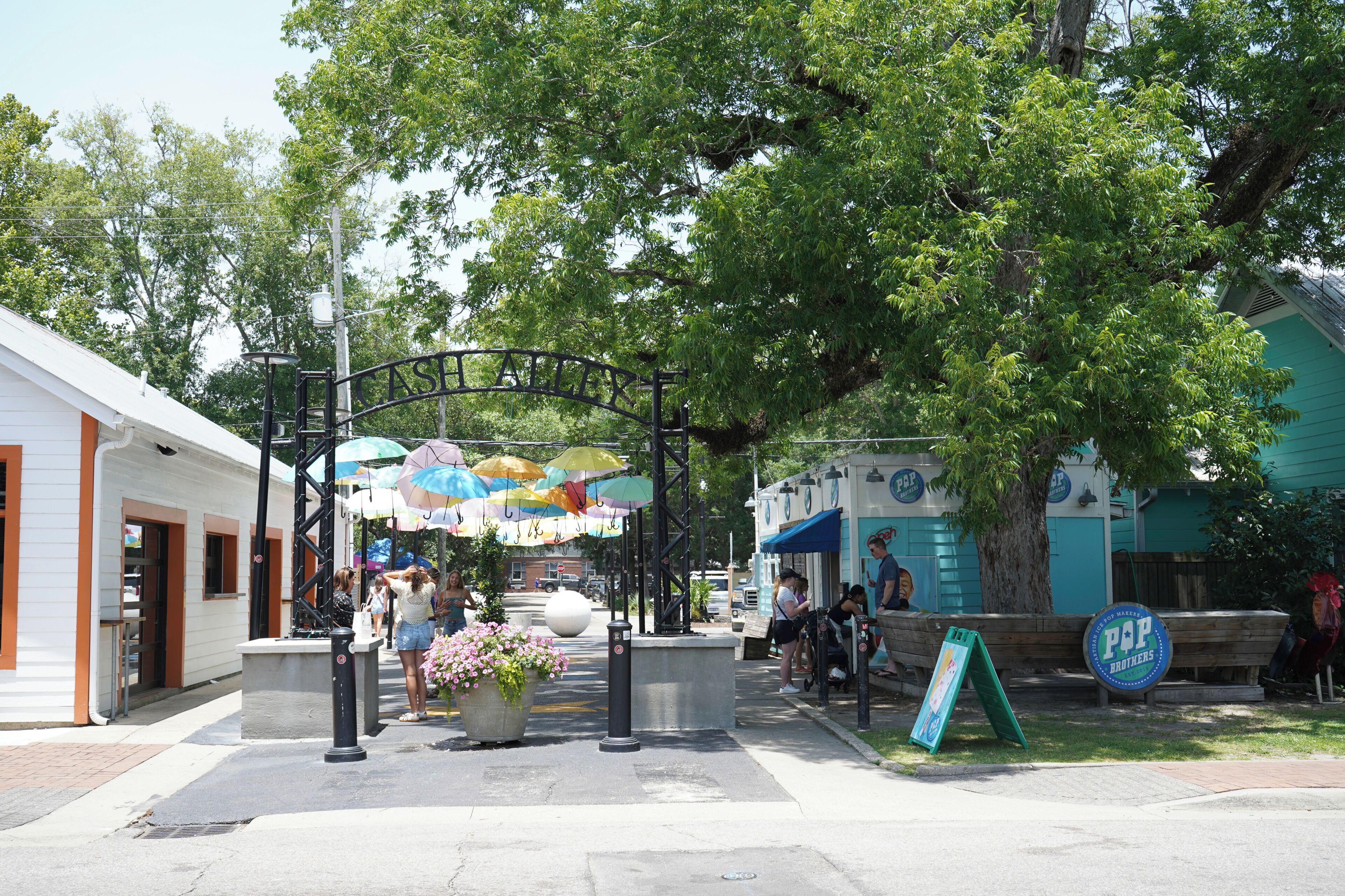 A street with a covered area, a sign for 'P&P Brothers,' and a large planter with flowers.