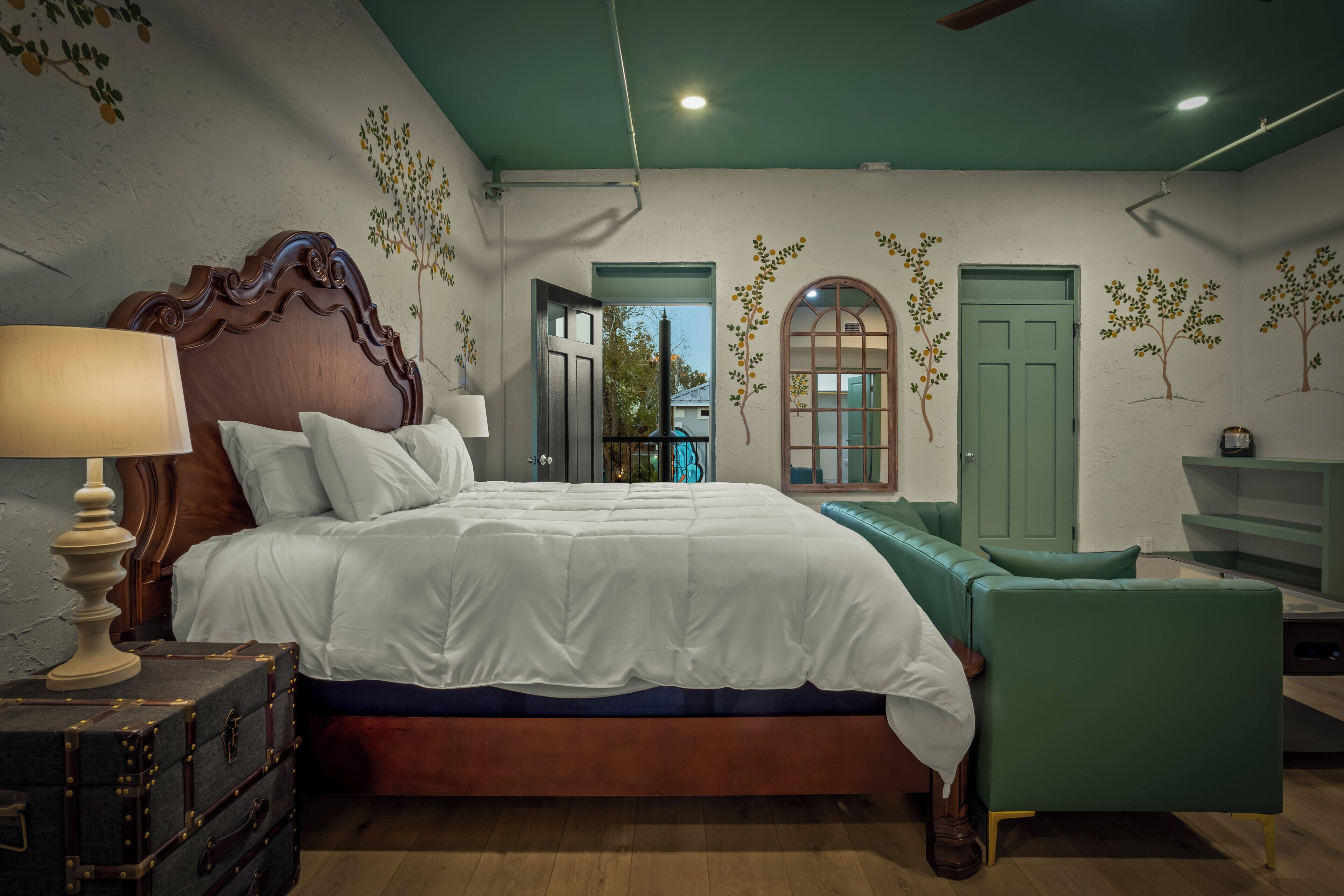 A bedroom with a large bed, a green sofa, a wooden headboard, and a lamp.