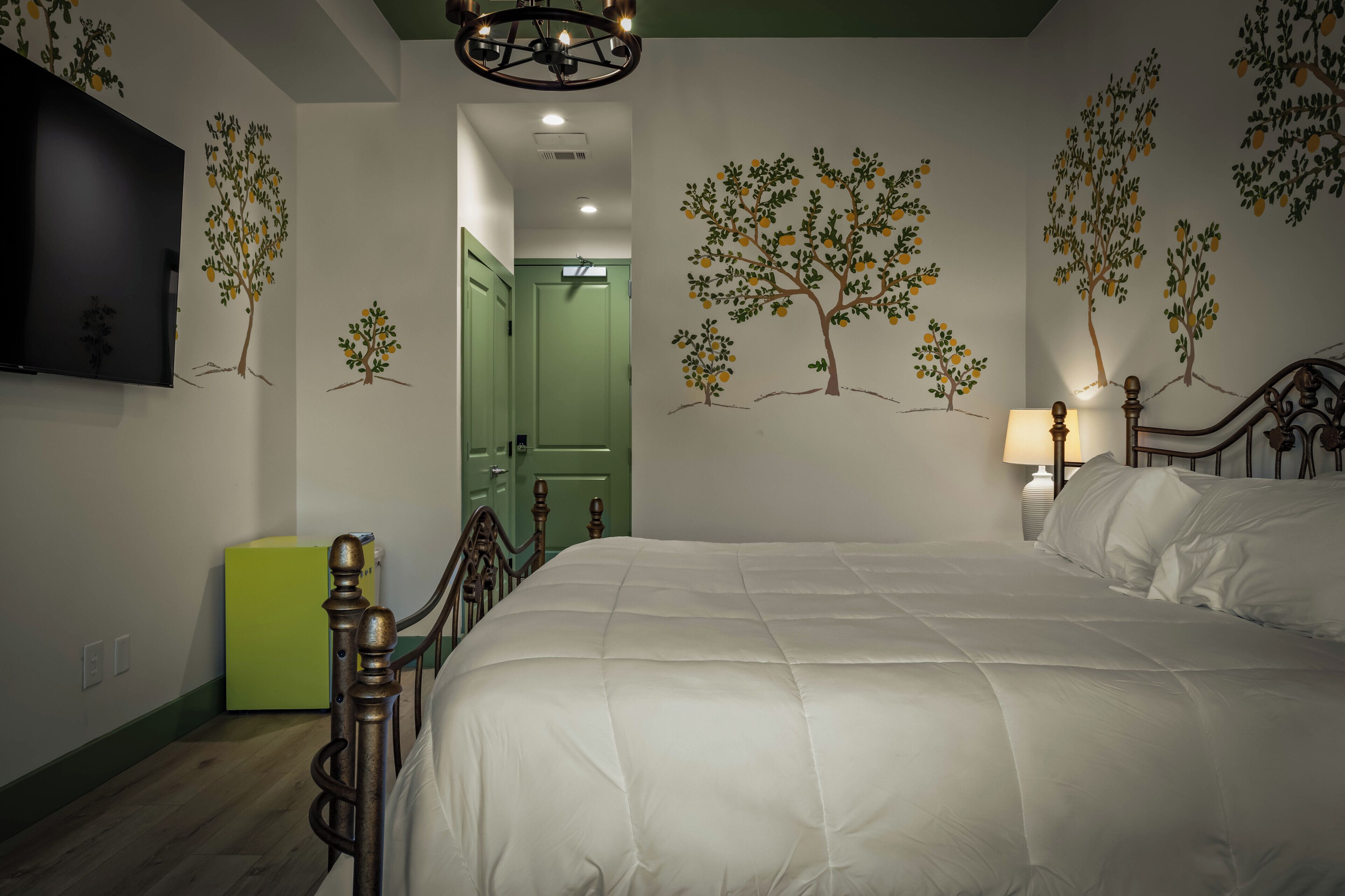 Un dormitorio con una cama, un televisor montado en la pared y una puerta que da a otra habitación.
