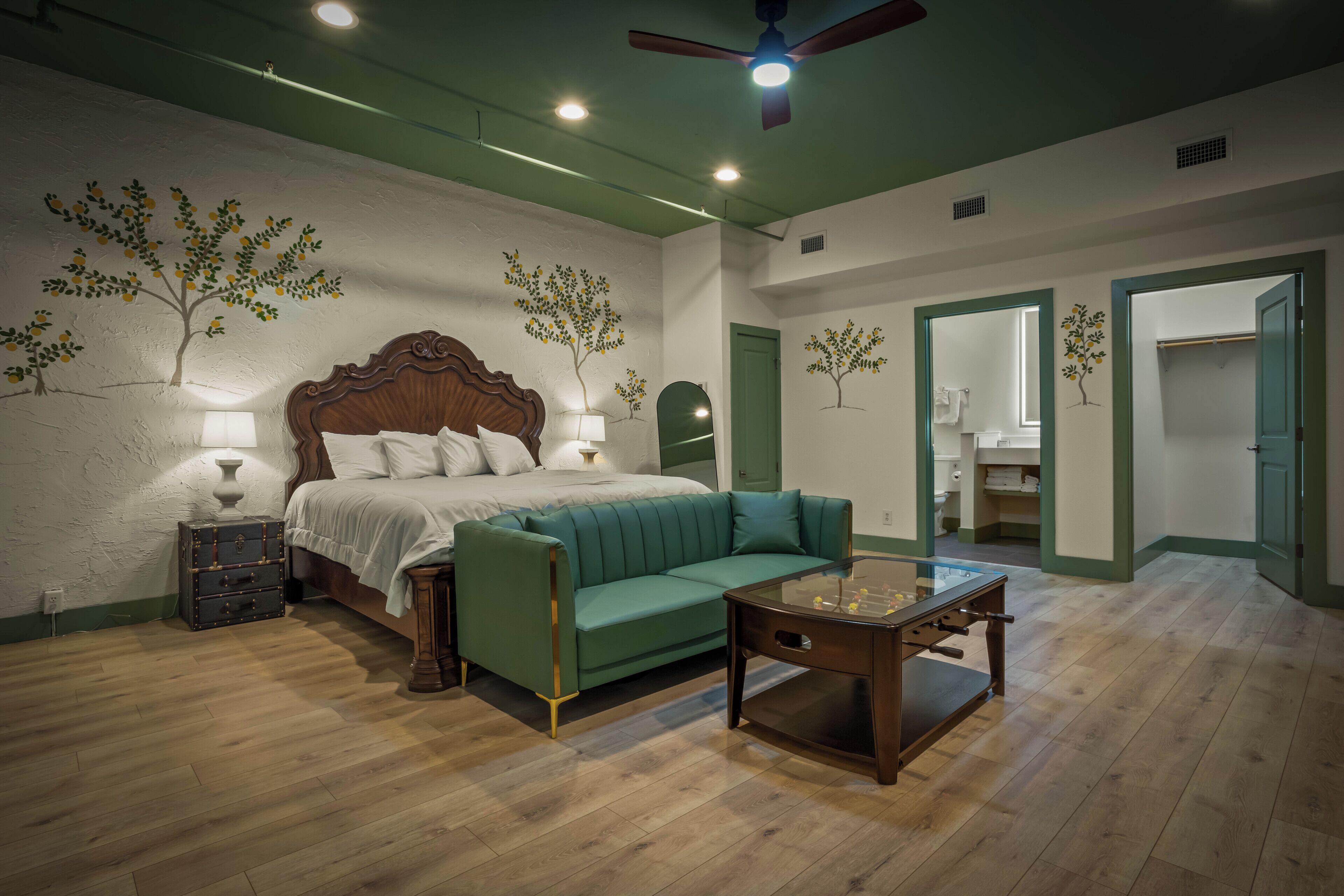 Un dormitorio con una cama, un sofá verde, una mesita de noche de madera y una mesa con una lámpara.
