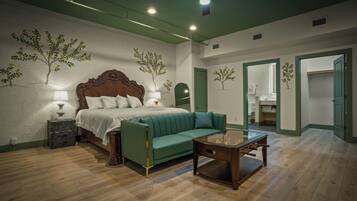 Un dormitorio con una cama, un sofá verde, una mesita de noche de madera y una mesa con una lámpara.