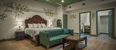 Un dormitorio con una cama, un sofá verde, una mesita de noche de madera y una mesa con una lámpara.