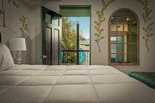 Un dormitorio con cama, lámpara, banca verde, puerta y ventana con vista a árboles.