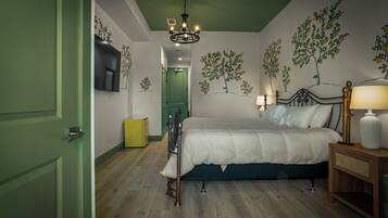Un dormitorio con cama, lámparas de noche, mesita de noche, una puerta verde y un muro con murales de árboles.