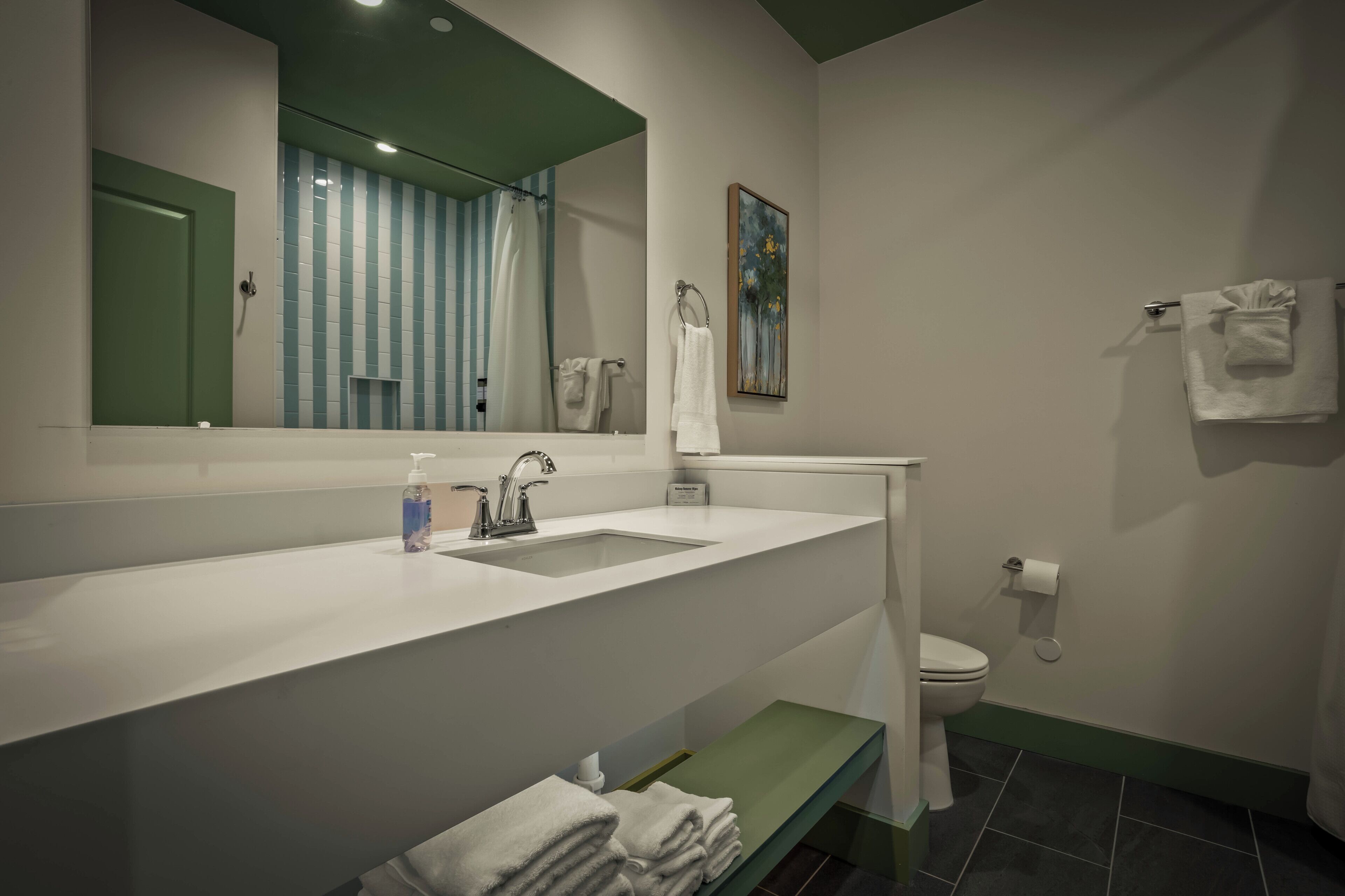 Un baño moderno con un lavamanos blanco, un banco verde, un inodoro y un espejo.
