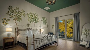 A bedroom with a bed, nightstands, a chandelier, a large window with a view, and wall art. - Hotel Mojo (Ocean Springs)