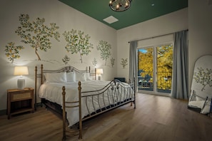Ein Schlafzimmer mit einem Bett, Nachttischen, einer Chandelier, einem großen Fenster mit Blick und Wandbildern.