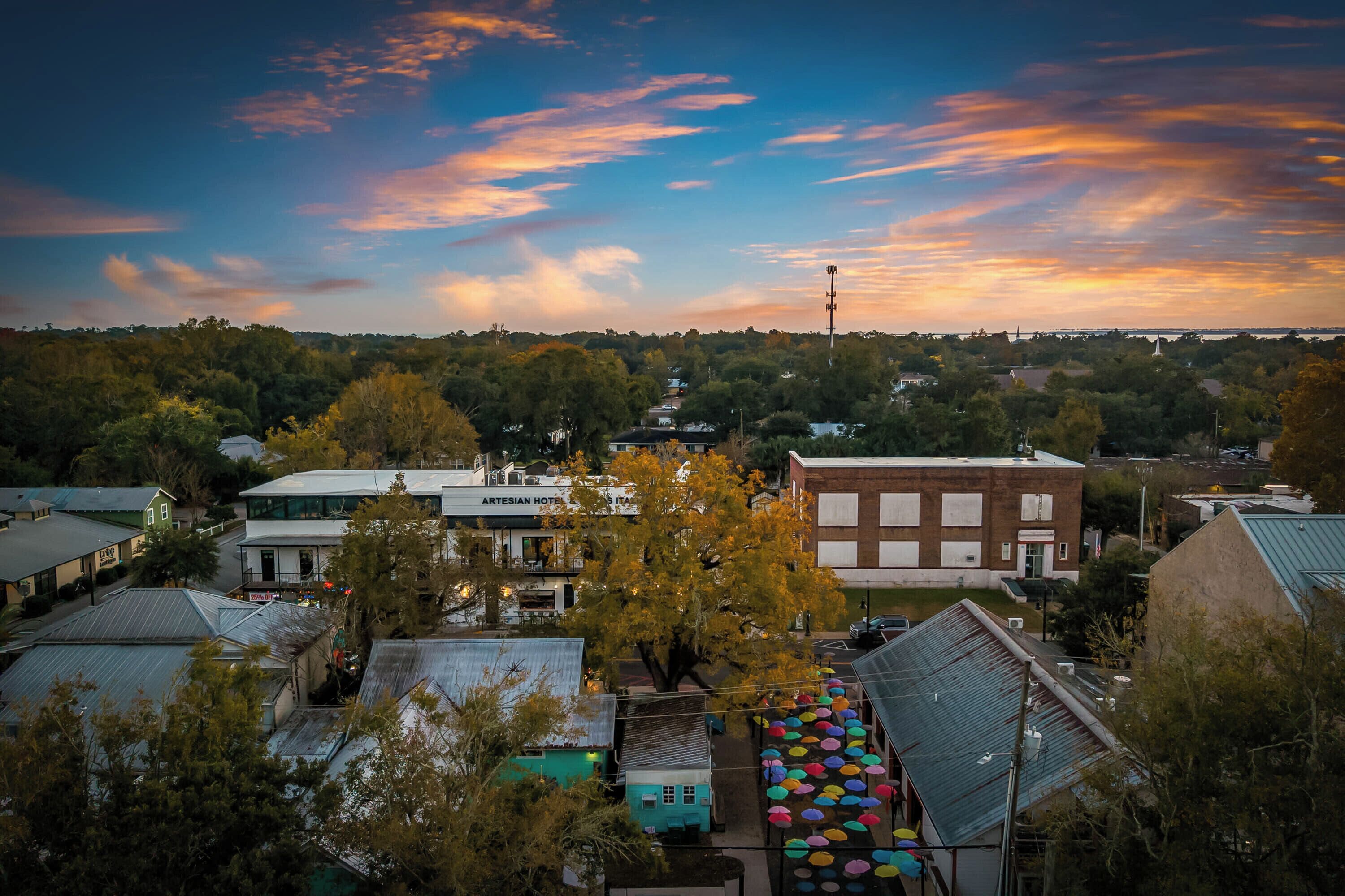 A town with buildings, including a hotel with a sign, surrounded by trees and a colorful sky.