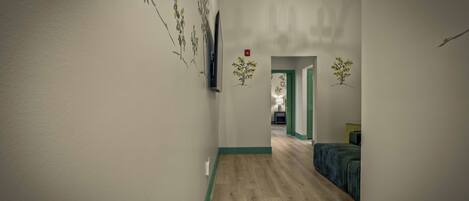 A hallway with a wooden floor, a bed with a striped bedspread, and wall art depicting trees.