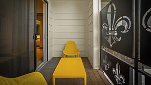 A yellow bench and chair in a narrow corridor with a wooden floor, a glass door, and a decorative black panel with fleur-de-lis designs. - Hotel Mojo (Ocean Springs)
