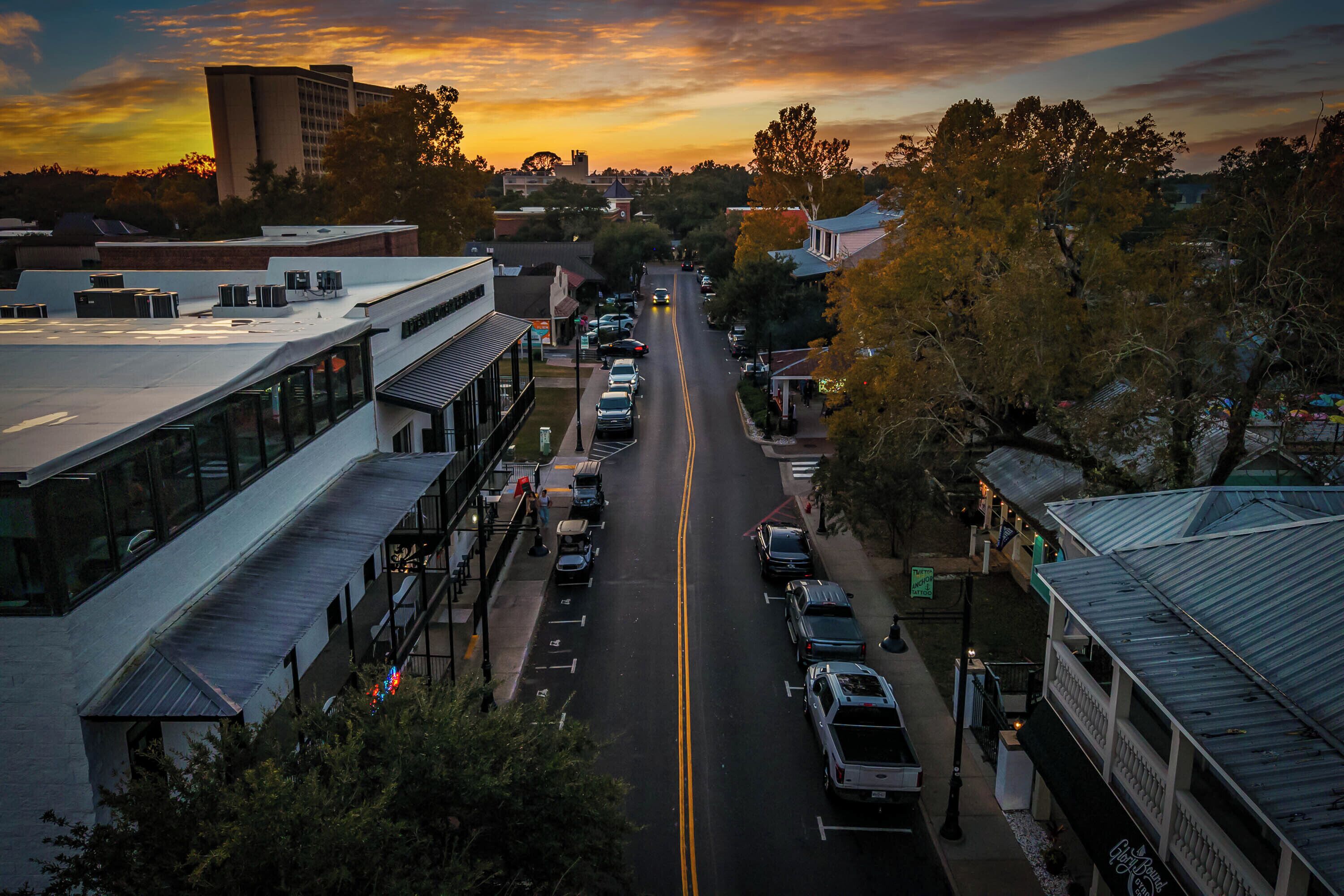 A street view with buildings, parked cars, and a clear sky.