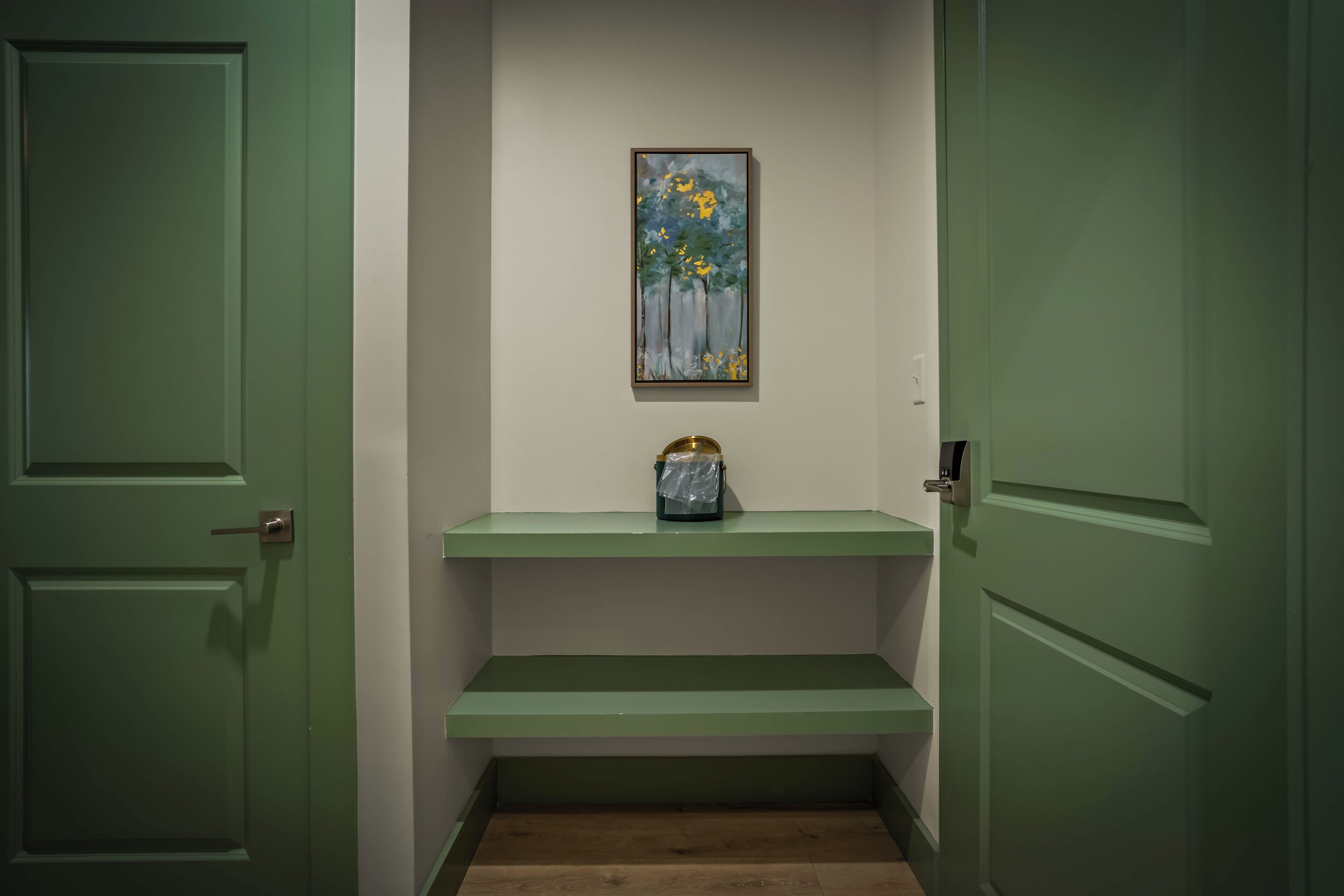 Un corridoio con porte verdi, un quadro appeso al muro e una piccola mensola con una borsa.