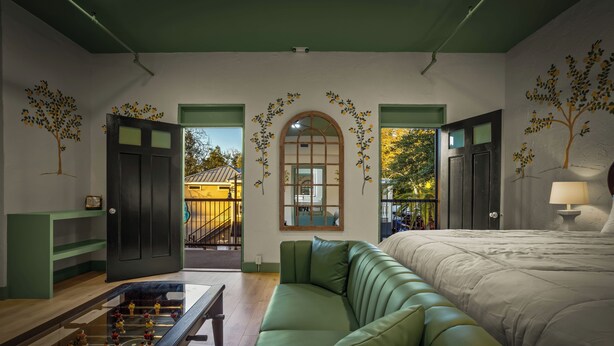 A room with a green sofa, a bed, a foosball table, and a view of a building outside. - Hotel Mojo (Ocean Springs)